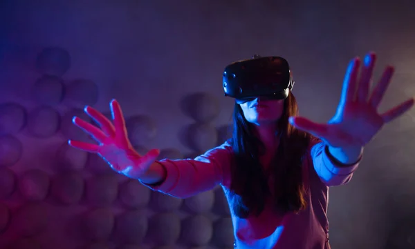A surprised woman in virtual reality glasses touches the air, tries to find something, uses an invisible control panel.