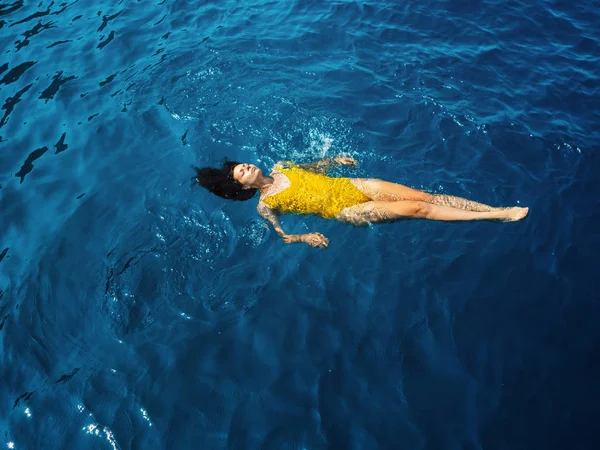 Молодая женщина в цельном желтом купальнике плавает на поверхности воды . — стоковое фото