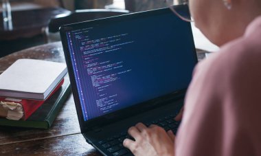 Hack sistemi. Koyu saçlı ve pembe kazak ve gözlük ile Heyecanlı kız bir kütüphanede bir dizüstü bilgisayarda kod yazıyor.