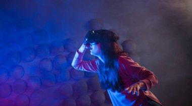 Sanal gerçeklik gözlüklerinde şaşırmış bir kadın havaya dokunur, bir şey bulmaya çalışır, görünmez bir kontrol paneli kullanır.