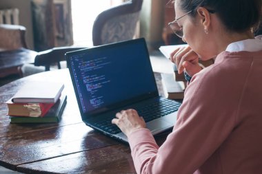 Hack sistemi. Koyu saçlı ve pembe kazak ve gözlük ile Heyecanlı kız bir kütüphanede bir dizüstü bilgisayarda kod yazıyor.
