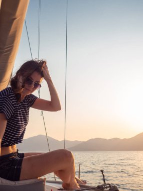 çizgili bir t-shirt çekici genç kadın bir yelkenli yat güvertesinde gün batımı sahiptir. Yelkenli yarış