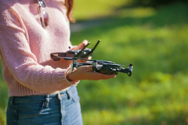 Una joven en un claro en un parque lanza, comprueba, sostiene un dron, en una mano, en el otro panel de control . —  Fotos de Stock