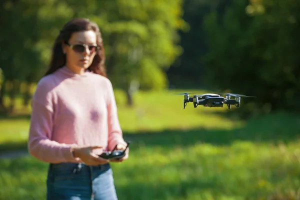 El dron de cuatro hélices flotaba en el aire a nivel de los ojos. La mujer está vigilando su vuelo con un panel de control . —  Fotos de Stock