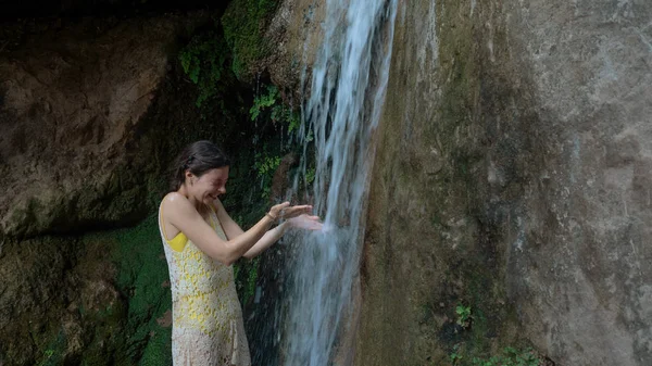 Girl washes her face under the waterfall in the woods. Young woman in swimsuit in mountain river — Zdjęcie stockowe