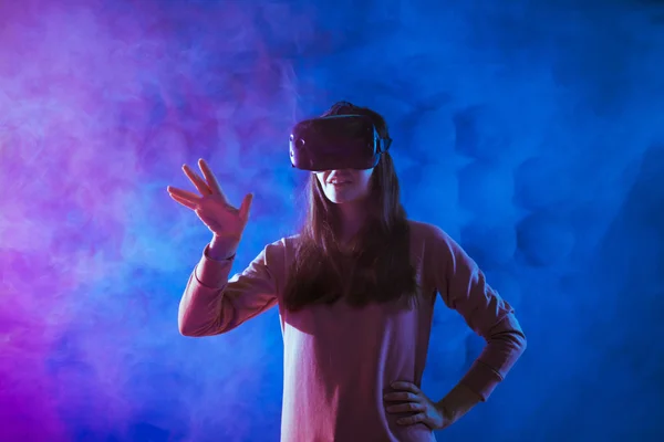 Mulher jovem surpreendente tocando o ar durante a experiência VR contra neon e fumaça de fundo futurista . — Fotografia de Stock
