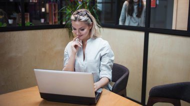 Bir ofis çalışanı ya da öğrenci bir dizüstü bilgisayar üzerinde çalışıyor. Şık bir ofiste kendine güvenen mutlu bir sarışın..