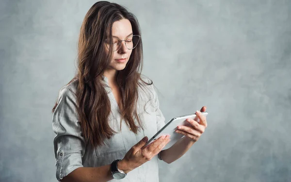 Joven mujer segura de éxito en una camisa gris utiliza una tableta digital para el trabajo y el acceso a Internet — Foto de Stock