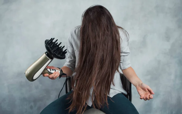 Eine junge Frau mit langen dunklen Haaren benutzt einen Föhn, um zu trocknen und zu stylen. Frisurenstyling und Haarpflege, — Stockfoto