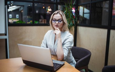 Bir ofis çalışanı ya da öğrenci bir dizüstü bilgisayar üzerinde çalışıyor. Şık bir ofiste kendine güvenen mutlu bir sarışın..
