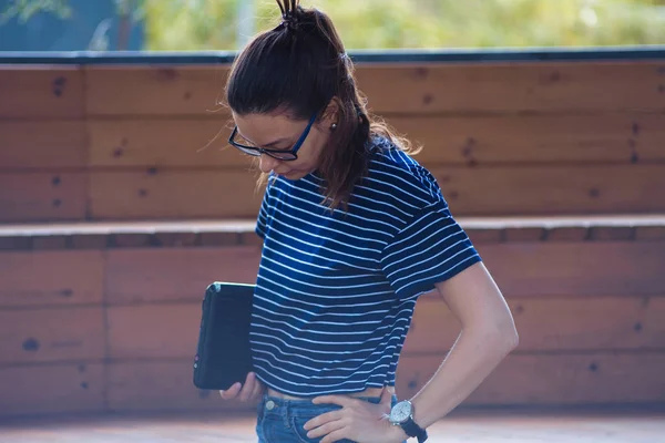 Jonge vrouw, staat op de achtergrond van houten treden, het vasthouden van de laptop, denken, rusten, kijkt naar het frame. — Stockfoto