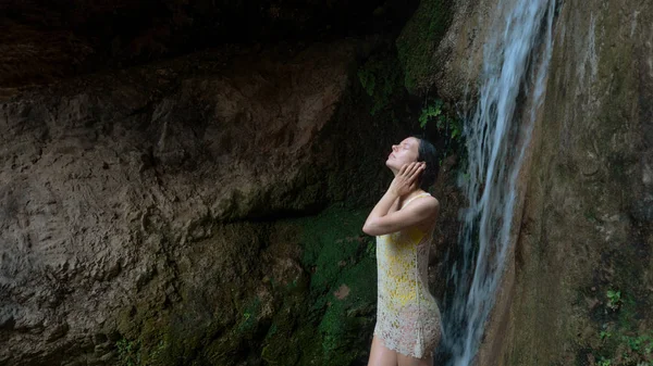Девушка умывается под водопадом в лесу. Молодая женщина в купальнике в горной реке — стоковое фото