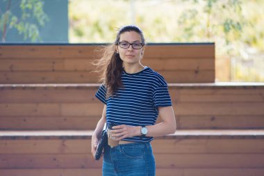 Genç bir kadın, ahşap basamakların arkasında dizüstü bilgisayarını tutuyor, düşünüyor, dinleniyor, çerçeveye bakıyor..