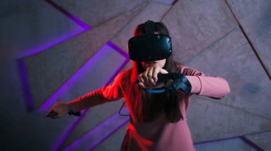 Kılıç kullan. Sanal kasklı genç bir kadın, sanal kılıçların kolları gibi her iki elinde de kontrolörler kullanır..