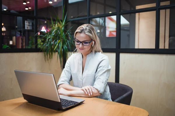 Jovem mulher em fones de ouvido sem fio senta-se em um laptop e trabalha ou se comunica na rede . — Fotografia de Stock