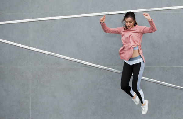 An athletic young woman is jumping, doing acrobatics, ballet, is actively involved in sports, against a concrete wall.