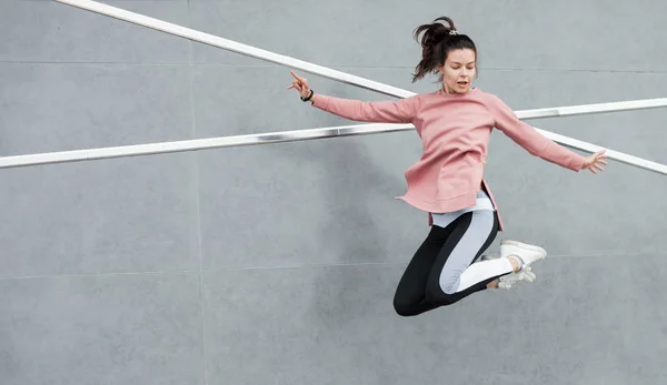 Een atletische jonge vrouw springt, doet acrobatiek, ballet, is actief betrokken bij sport, tegen een betonnen muur. — Stockfoto