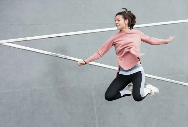 Een atletische jonge vrouw springt, doet acrobatiek, ballet, is actief betrokken bij sport, tegen een betonnen muur. — Stockfoto