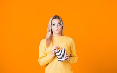 Sarı kazaklı, neşeli genç bir kadın film izliyor ve patlamış mısır yiyor..