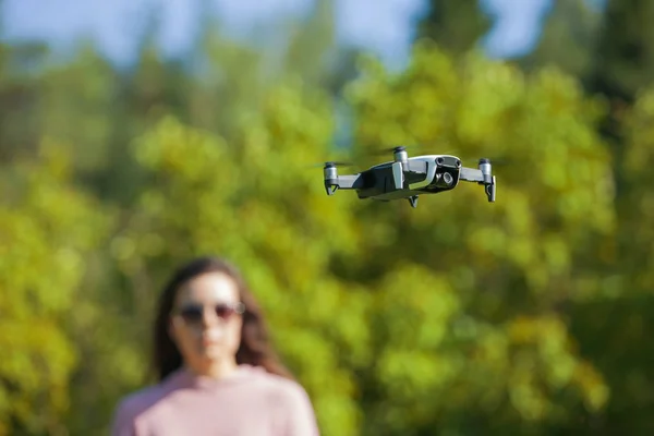 Il drone a quattro eliche aleggiava nell'aria a livello degli occhi. Donna in occhiali da sole e un maglione rosa a guardare il suo volo . — Foto Stock