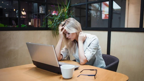 Stressige junge Geschäftsfrau sitzt am Tisch und arbeitet an einem problematischen Thema — Stockfoto