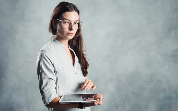 Morena en gafas y una camisa gris con una tableta digital en sus manos , — Foto de Stock