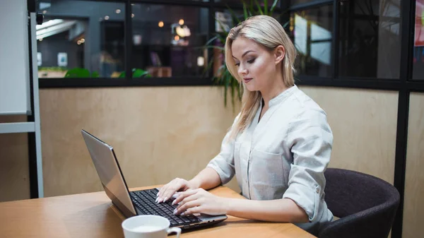 Egy irodai dolgozó vagy diák egy laptopon dolgozik. Boldog magabiztos szőke egy elegáns irodában. — Stock Fotó