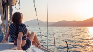 çizgili bir t-shirt çekici genç kadın bir yelkenli yat güvertesinde gün batımı sahiptir. Yelkenli yarış