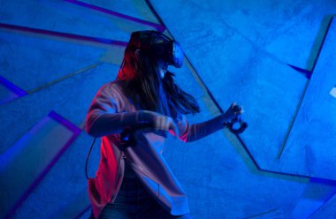 Kılıç kullan. Sanal kasklı genç bir kadın, sanal kılıçların kolları gibi her iki elinde de kontrolörler kullanır..