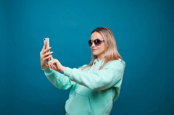 Loura alegre com um telefone celular. Retrato de uma jovem mulher positiva com capuz azul — Fotografia de Stock