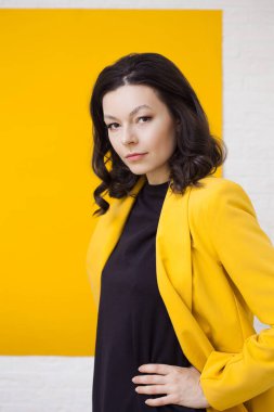 Sarı arka planda sarı ceketli şık bir genç kadın.,