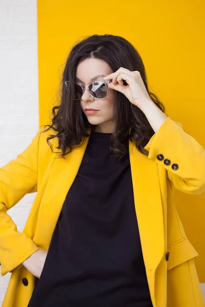 Stylische und gewagte junge Brünette in leuchtend gelber Jacke und verspiegelter Sonnenbrille. — Stockfoto