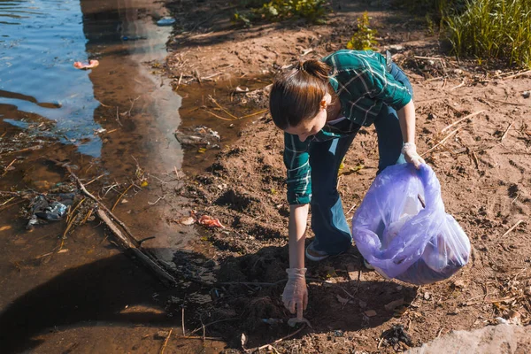 Грязный берег реки, много мусора в природе. Молодая женщина-волонтер — стоковое фото