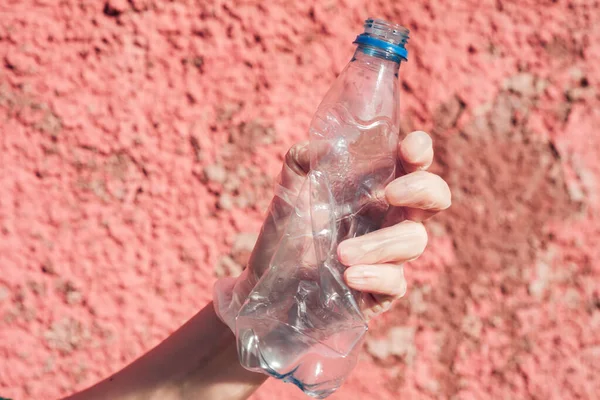 We are against plastic garbage. A hand in protective gloves clutches an empty disposable bottle.
