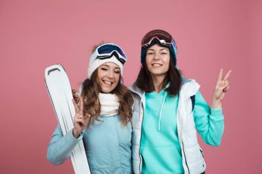 Pembe arka planda kışlık elbiseli iki komik arkadaş. İki kayakçı.