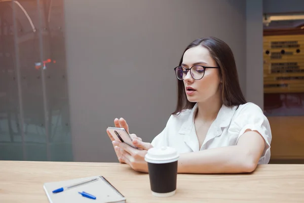 Joven hermosa mujer en gafas y una blusa blanca está sentado en un espacio público — Foto de Stock