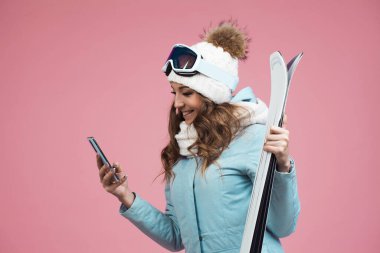 Kayaklı genç bir kadın kayak koşularını planlamak için akıllı telefon kullanıyor. Bir kayak merkezinde kış tatili