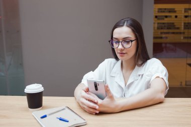 Öğrenci kız masada oturuyor ve akıllı telefonunda bir uygulama kullanıyor..
