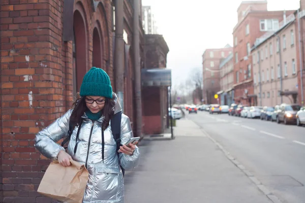 Kurier oder freiwilliger Helfer trägt Lebensmittel in einer Papiertüte. Eine junge Frau in einer warmen Jacke — Stockfoto