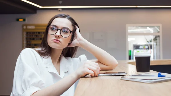 young beautiful woman in glasses and a white blouse is sitting in a public space