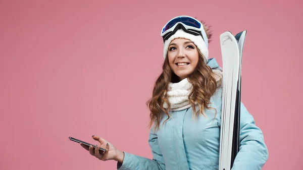 Jeune femme avec des skis utilise un smartphone pour planifier ses pistes de ski. Vacances d'hiver dans une station de ski — Photo