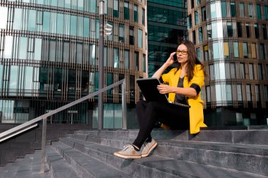 Dizüstü bilgisayarlı serbest çalışan iş merkezinin yanındaki merdivenlerde oturuyor.,