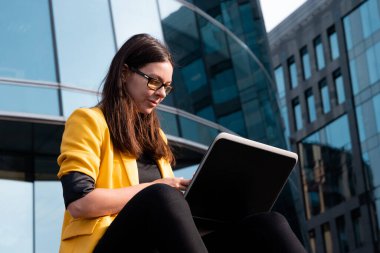 İş merkezinin yanındaki basamaklarda dizüstü bilgisayarı olan serbest çalışan biri oturuyordu.,