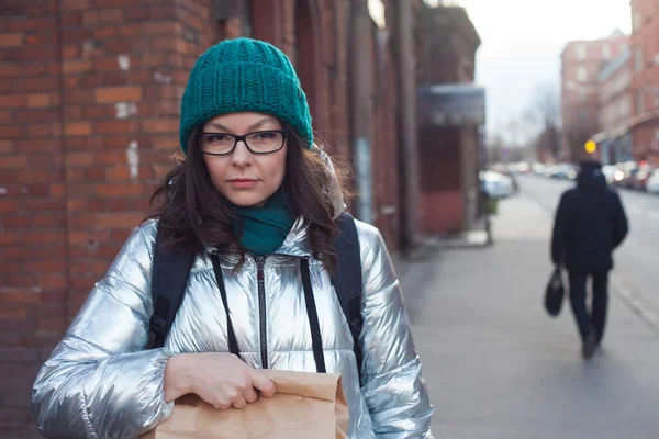 Jonge vrouw in warme kleren met een papieren zak in haar handen, gaan winkelen. — Stockfoto