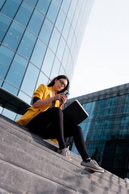 İş merkezinin yanındaki basamaklarda dizüstü bilgisayarı olan serbest çalışan biri oturuyordu.,