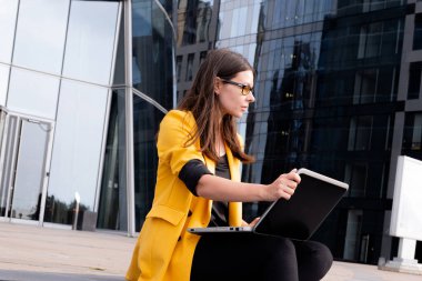 İş merkezinin yanındaki basamaklarda dizüstü bilgisayarı olan serbest çalışan biri oturuyordu.,