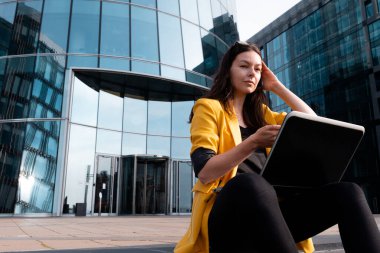 İş merkezinin yanındaki basamaklarda dizüstü bilgisayarı olan serbest çalışan biri oturuyordu.,