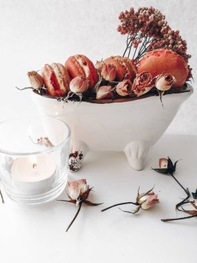 beyaz bir arka plan mum üzerinde kuru çiçekler ile bir tabak üzerinde bir vazo pembe macaroons