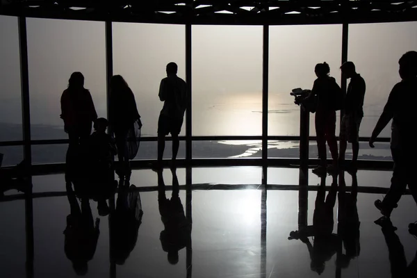 Силуэты людей в аэропорту на фоне панорамного стекла на закате — стоковое фото