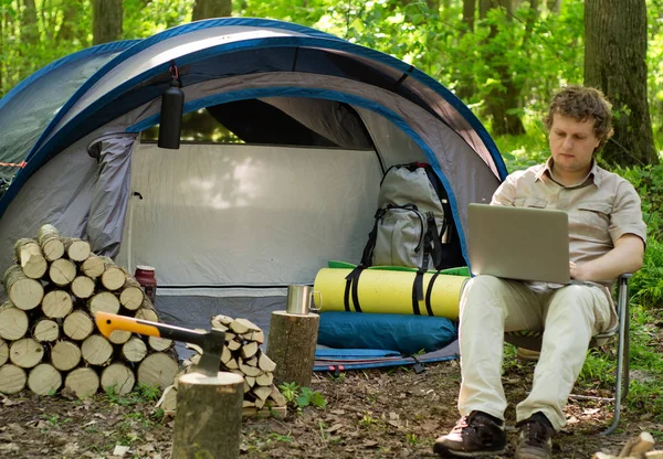 A man working on a laptop outdoors in a tent camp.